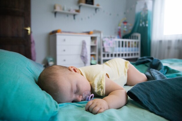 il bambino dorme su un grande letto sullo sfondo di una culla e una cassettiera