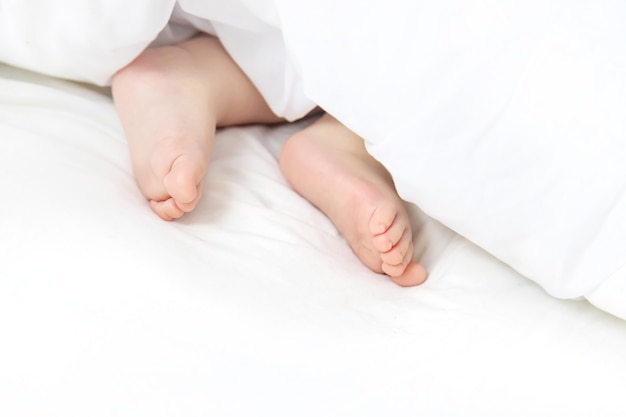 Il bambino dorme su un letto bianco con i suoi piedi