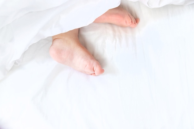 Il bambino dorme su un letto bianco con i suoi piedi