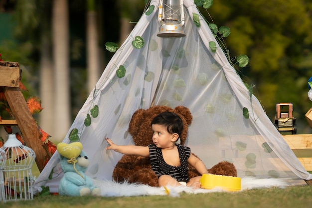 il bambino è felice di giocare con l'orsacchiotto e i giocattoli seduti all'interno di una piccola tenda in giardino