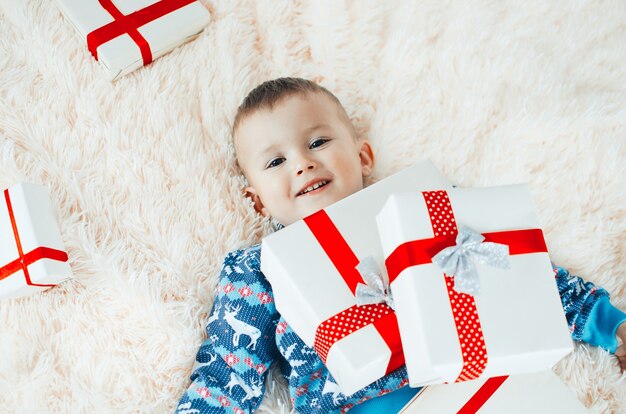 Il bambino è sdraiato sulla soffice coperta soffice, accanto a lui un mucchio di regali, il bambino è molto felice