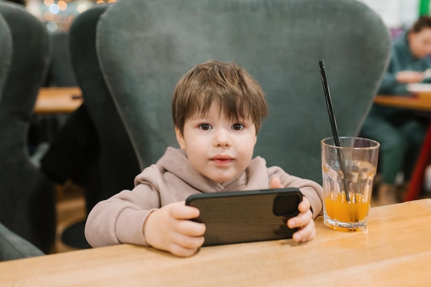 Il bambino è seduto a un tavolo in un bar e tiene in mano uno smartphone