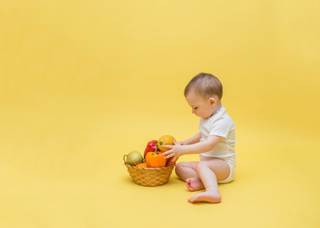 Il bambino è seduto con un cesto di frutta e verdura. Il bambino sta smistando un cesto di frutta e verdura su uno spazio giallo. Copia spazio