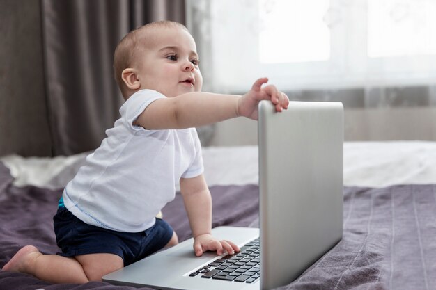 Il bambino è seduto sul letto con un computer portatile. Nuova generazione.