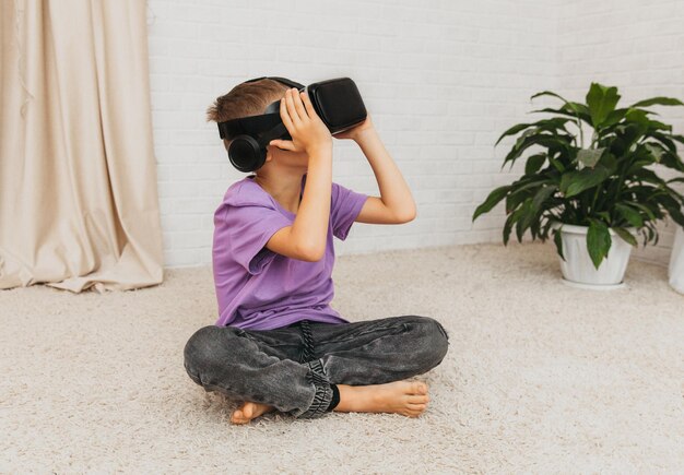 Il bambino eccitato con gli occhiali per realtà virtuale si siede sul pavimento a casa.