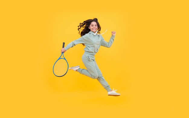 Il bambino energico felice salta in abbigliamento sportivo con la racchetta da squash che corre verso il successo su sfondo giallo, successo sportivo.