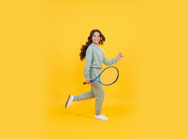 Il bambino energico felice salta in abbigliamento sportivo con la racchetta da tennis che corre verso il successo su sfondo giallo, infanzia attiva.