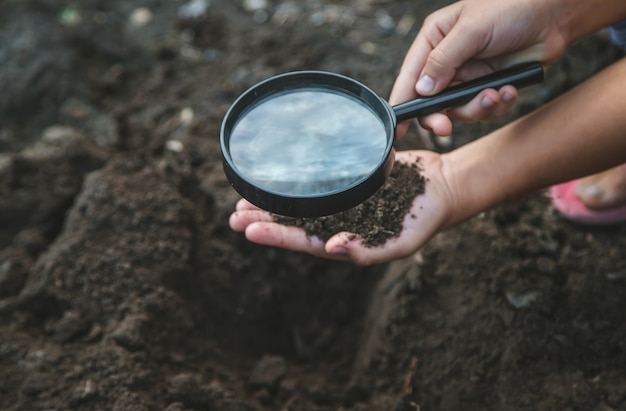 Il bambino esamina il terreno con una lente d'ingrandimento. Messa a fuoco selettiva.