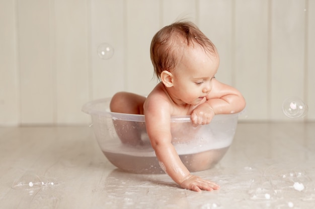 Il bambino fa il bagno o si lava in una bacinella con schiuma e bolle di sapone