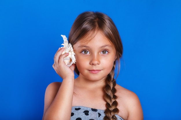 Il bambino felice ascolta la conchiglia. Vacanze estive e concetto di viaggio