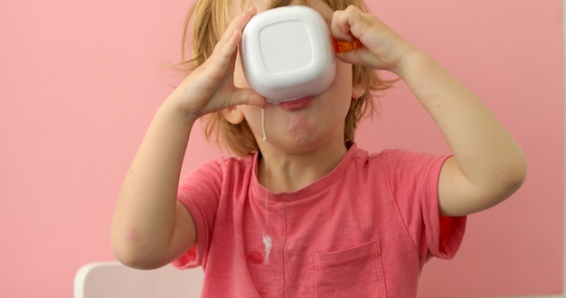 Il bambino felice beve il latte da una tazza