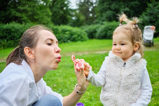 Il bambino felice con la mamma soffia bolle di sapone.