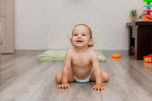Il bambino felice di 11 mesi striscia sul pavimento e ride. il bambino è seduto sul pavimento.