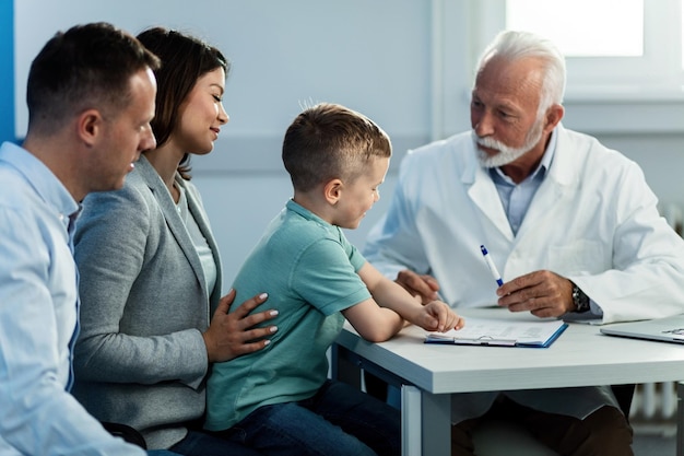 Il bambino felice e i suoi genitori si siedono nell'ufficio del medico e comunicano con il pediatra anziano L'attenzione è rivolta al ragazzo