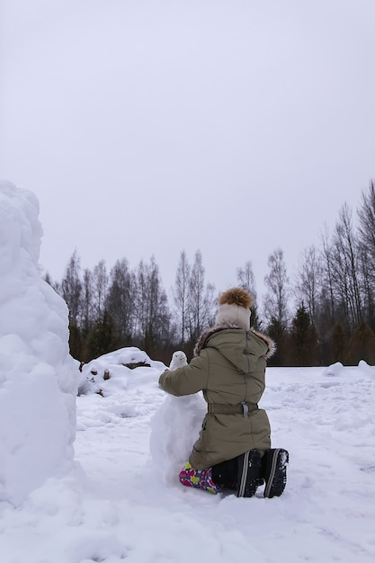 Il bambino felice fa un pupazzo di neve in un campo innevato in campagna.