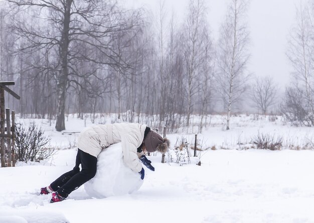 Il bambino felice fa un pupazzo di neve in un campo innevato in campagna.