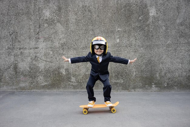 Il bambino felice finge di essere un uomo d'affari. Bambino divertente che guida lo skateboard all'aperto. Ritorno al lavoro, avvio e concetto di idea imprenditoriale