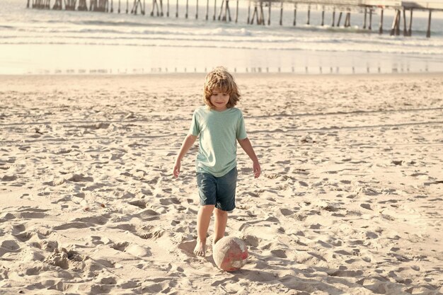Il bambino felice gioca con il pallone da calcio sulla spiaggia durante le vacanze estive