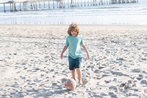 Il bambino felice gioca con il pallone da calcio sulla spiaggia durante le vacanze estive