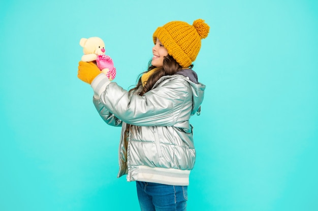 Il bambino felice in cappello e guanti tiene il giocattolo su sfondo blu, infanzia.