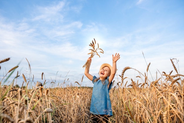 Il bambino felice nel campo di frumento tira le mani verso l'alto