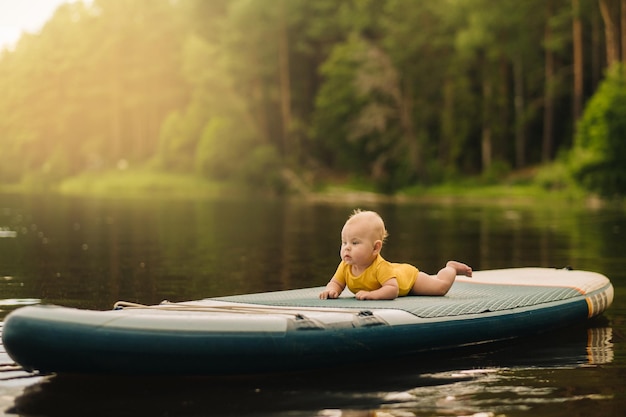 Il bambino giace galleggiante sull'acqua su una grande tavola da sup Sport acquatici