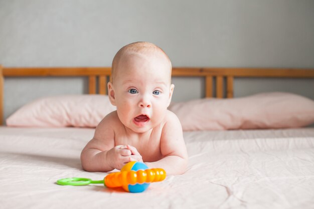 Il bambino giace sul letto sulla pancia e guarda con interesse il sonaglio colorato che le sta di fronte