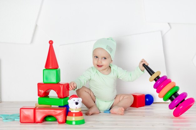 Il bambino gioca con i giocattoli nella stanza dei bambini a casa in un body verde, il concetto di sviluppo e tempo libero dei bambini piccoli