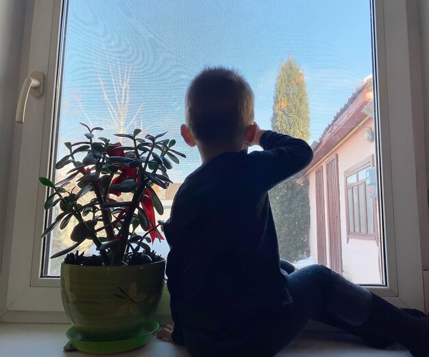 Il bambino guarda fuori dalla finestra e aspetta i genitori dal lavoro. Messa a fuoco selettiva.