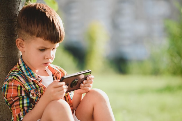 Il bambino guarda il cellulare mentre è seduto in estate per strada