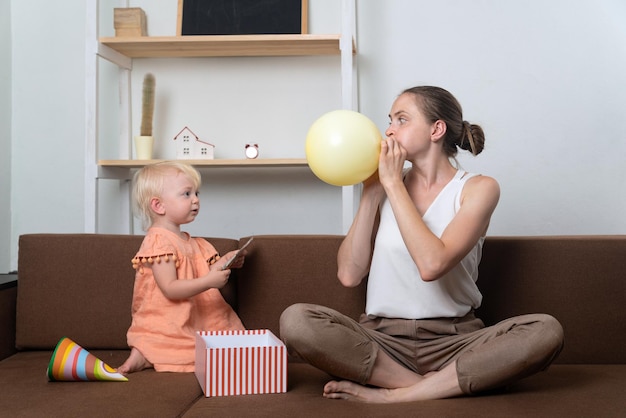 Il bambino guarda mentre la mamma fa esplodere il palloncino Babysitter e bambino a casa sul divano