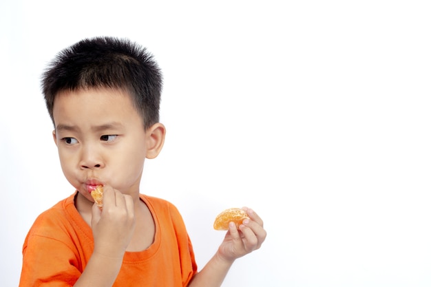 Il bambino in attrezzatura arancione mangia l&#39;arancia isolata su fondo bianco