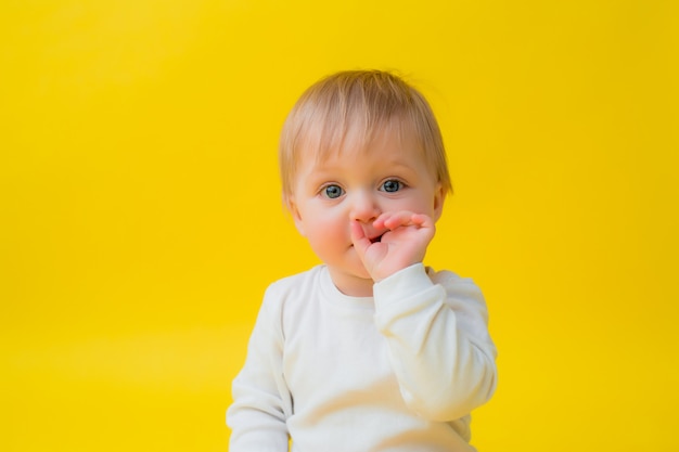 Il bambino in buona salute in tuta bianca si siede su una priorità bassa gialla, spazio per testo