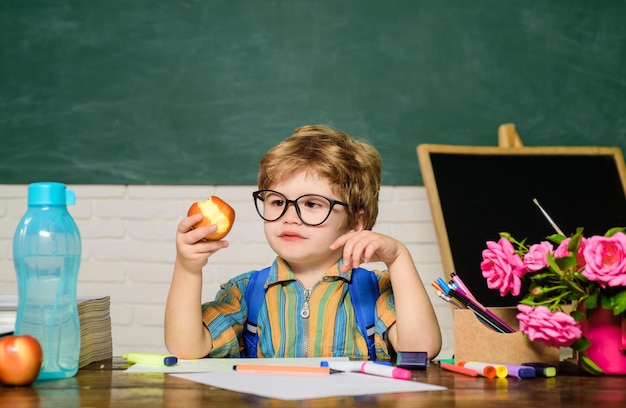 Il bambino in classe ha il pranzo scolastico lo scolaro all'ora di pranzo il ragazzino divertente con gli occhiali si siede alla scrivania