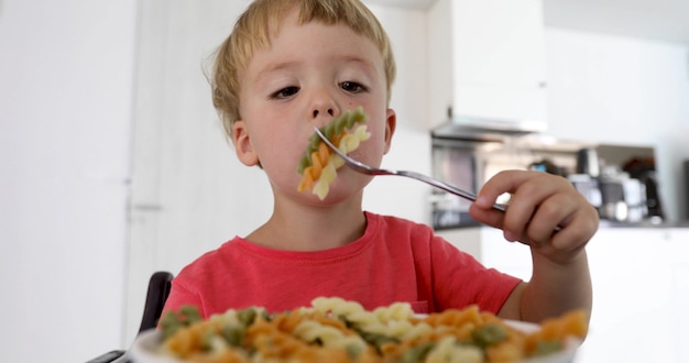 Il bambino in cucina a tavola mangiando maccheroni