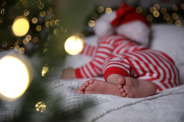 Il bambino in pigiama natalizio e cappello da Babbo Natale che dorme sul letto al chiuso si concentra sui piedi