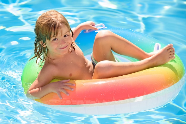 Il bambino in piscina si rilassa nuota su un anello gonfiabile e si diverte in acqua durante le vacanze estive bambino divertente...