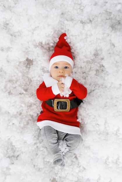 Il bambino in un costume da Babbo Natale si trova nella neve artificiale, vista dall'alto. Biglietto natalizio