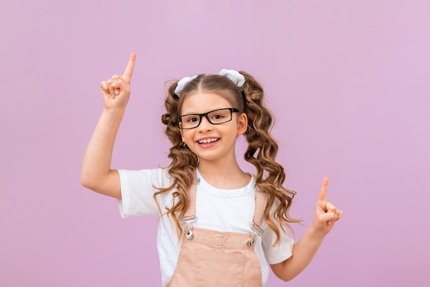 Il bambino indica l'annuncio. una ragazza con riccioli e occhiali su uno sfondo isolato. Il modello si presenta.