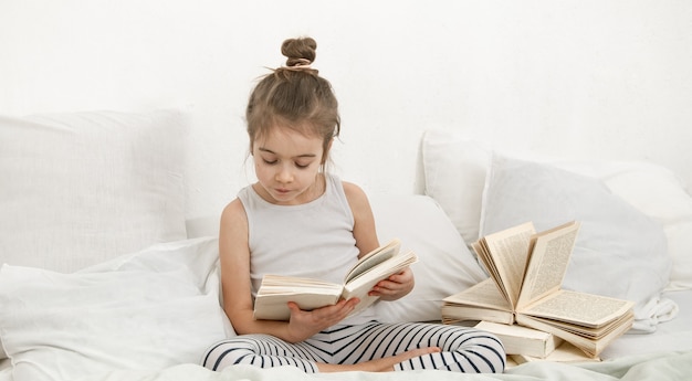 Il bambino legge un libro in pigiama su un letto. Lo sviluppo del bambino e lo spazio della copia del concetto di apprendimento.