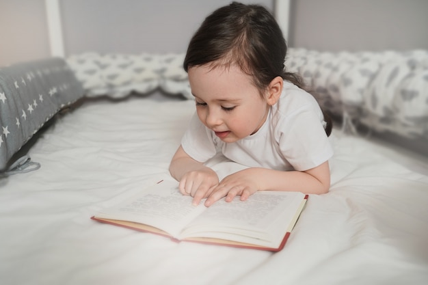 Il bambino legge un libro prima di andare a letto nel suo letto. La ragazza si nascose sotto le coperte e legge. Il bambino si nasconde in una coperta rosa.