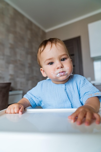 Il bambino mangia cibo in cucina Il bambino divertente e sporco mangia la panna acida sulla sedia