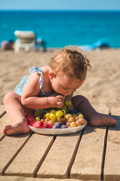 Il bambino mangia frutta in riva al mare. Messa a fuoco selettiva. Ragazzo.