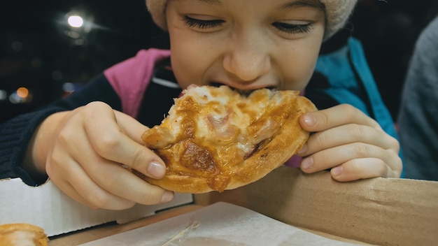 Il bambino mangia la pizza formaggio quattro Primo piano della bocca della donna della ragazza che mangia avidamente pizza e mastica nel ristorante all'aperto Mani dei bambini del capretto che prendono una fetta di pizza italiana calda e saporita dalla scatola aperta