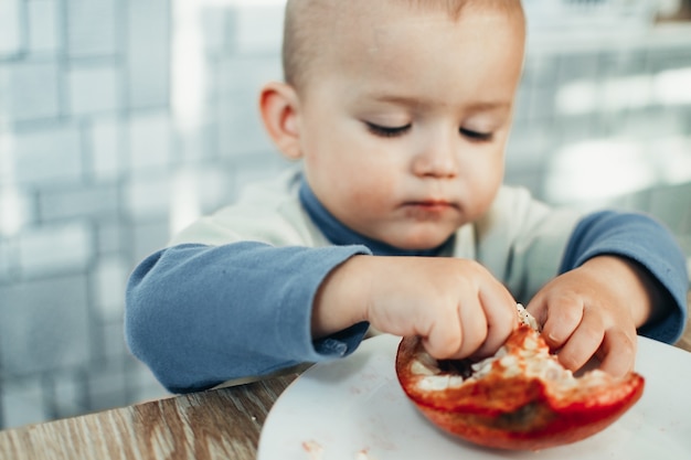 Il bambino mangia una melagrana, matura e succosa, molto gustosa e gioiosa