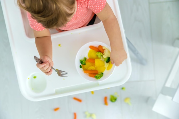 Il bambino mangia verdure su una sedia Messa a fuoco selettiva Bambino