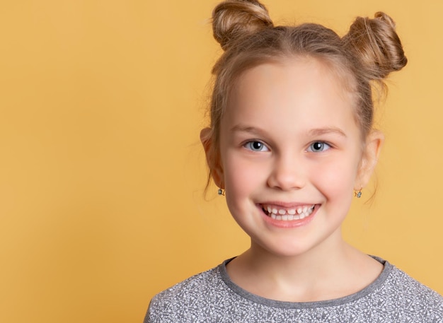 Il bambino mostra i suoi denti sani. Primo piano del volto di una bambina carina che sorride mostrando i denti su uno sfondo giallo. Concetto di odontoiatria pediatrica. Articolo. bandiera. Posto per il testo.