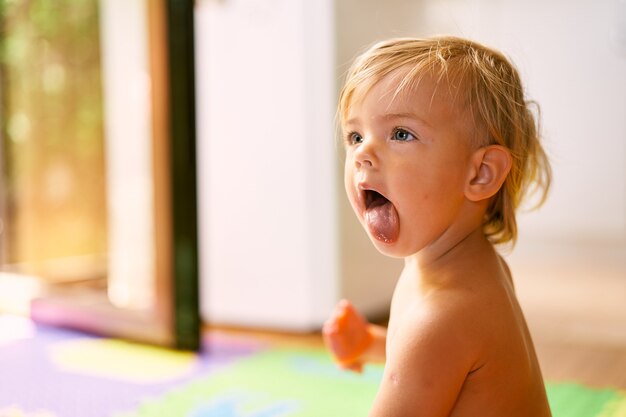 Il bambino mostra la lingua mentre è seduto sul pavimento nella stanza