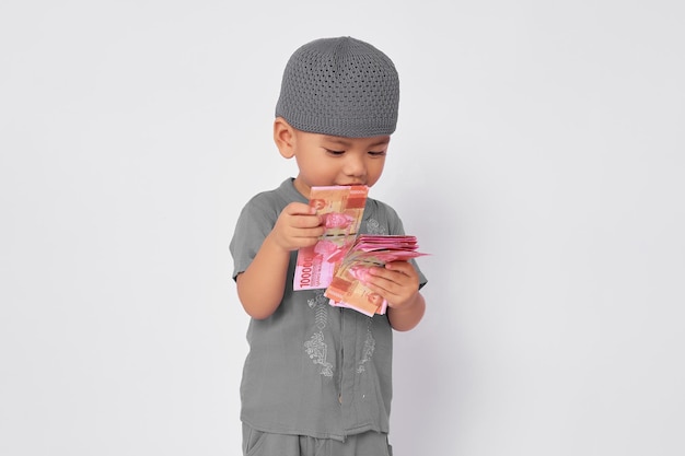 Il bambino musulmano asiatico eccitato riceve banconote piene di denaro contante durante l'Eid fitr isolato su sfondo bianco dello studio