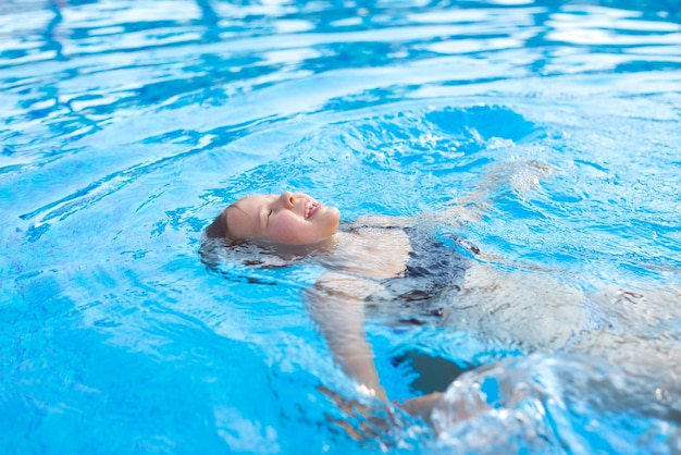 Il bambino nell'acqua blu della piscina si rilassa nuotando sulla schiena chiudi gli occhi